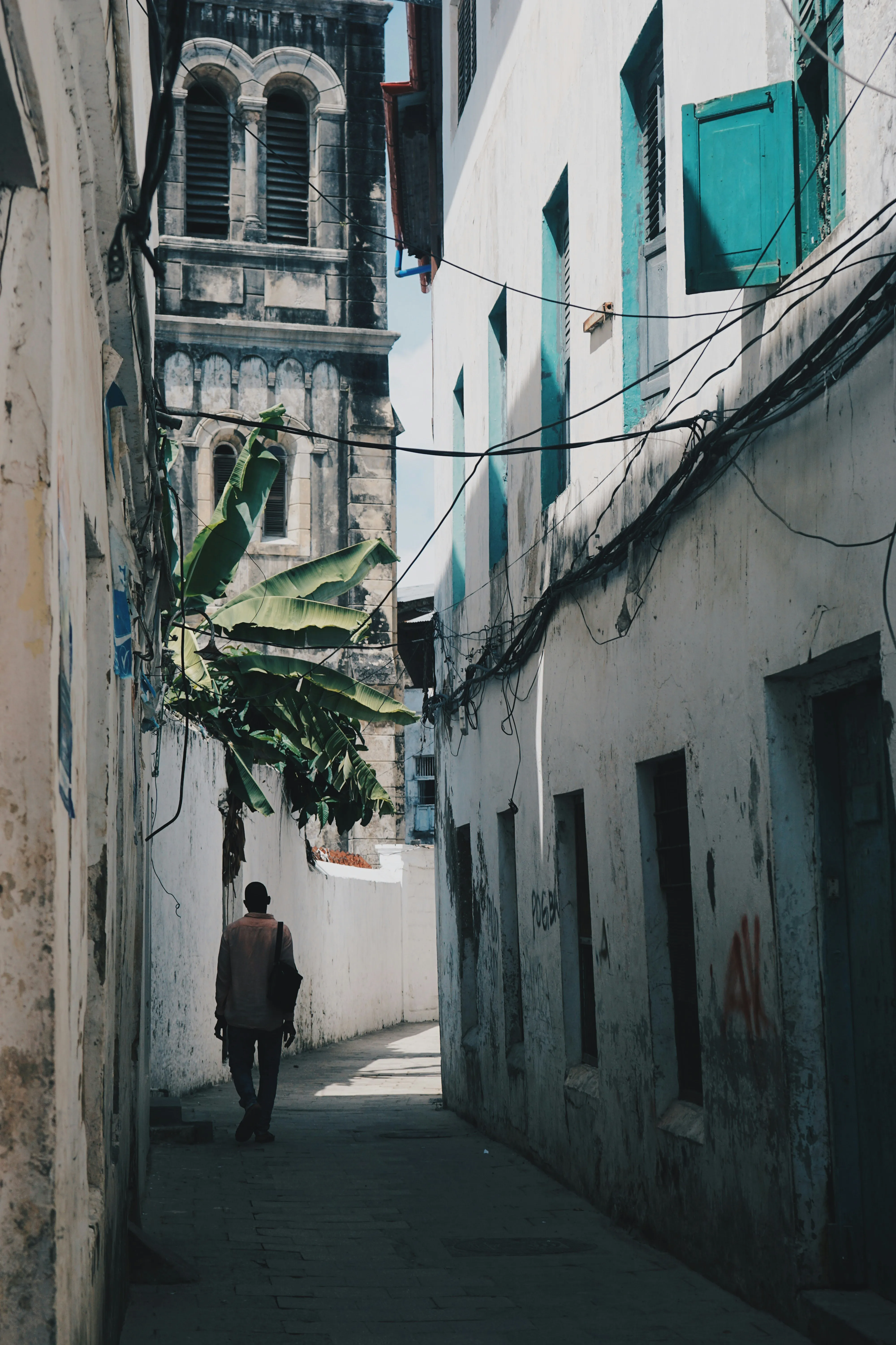 A narrow whitewashed alley in Stone Town with a stone bell tower and banana palms
