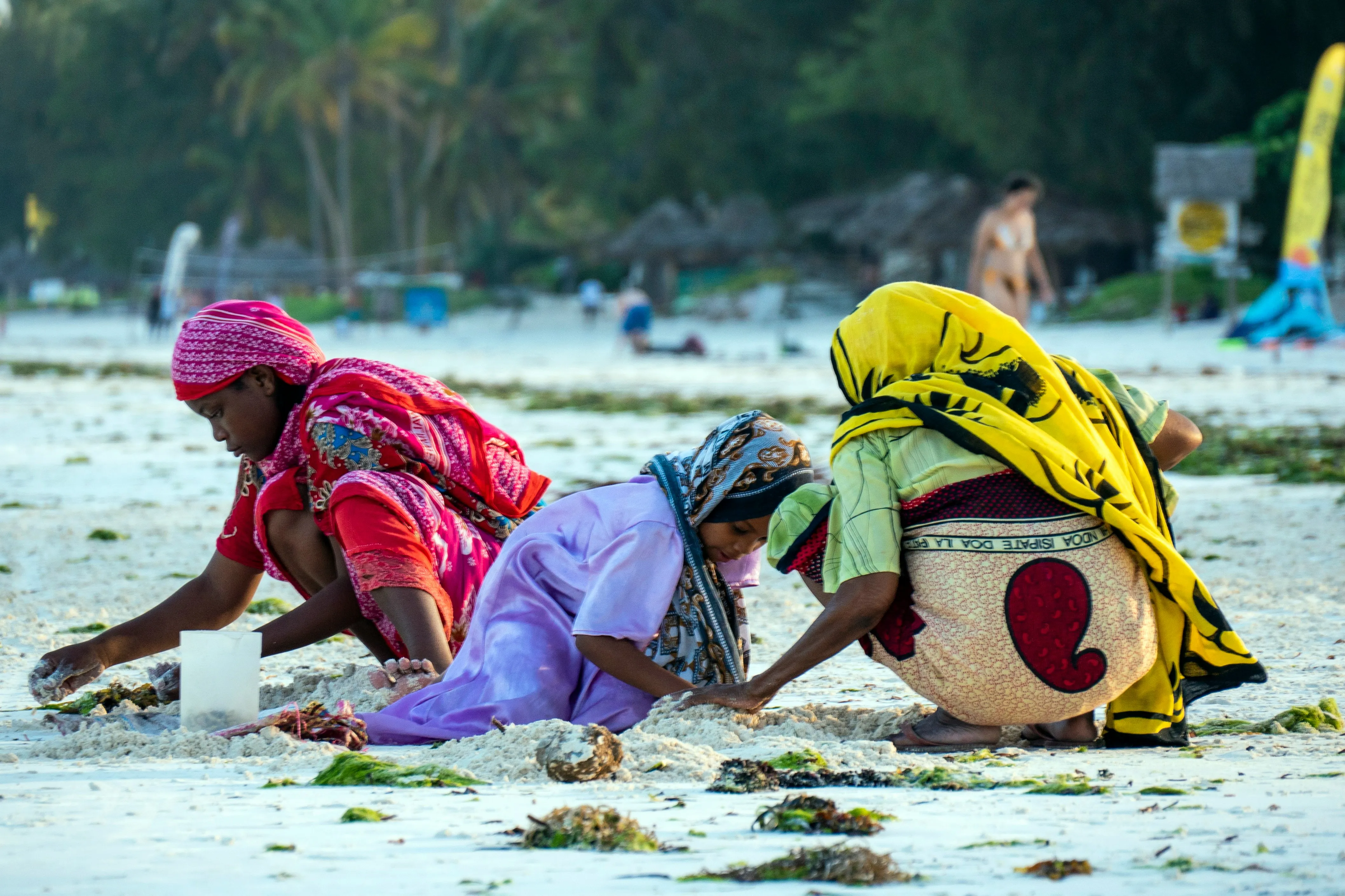 Three women in vibrant kangas gathering on a Zanzibar beach at low tide